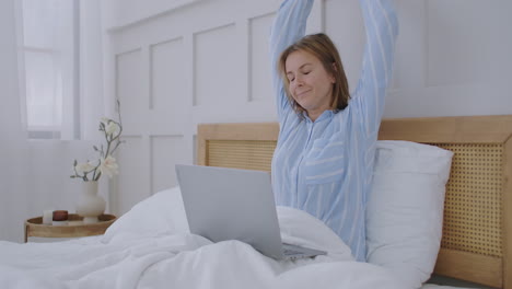 Young-Millennial-Girl-Sitting-on-a-Bed-in-the-Morning-Uses-Laptop-Computer.-caucasian-woman-home-urban-working-online-laptop-bedroom-bed